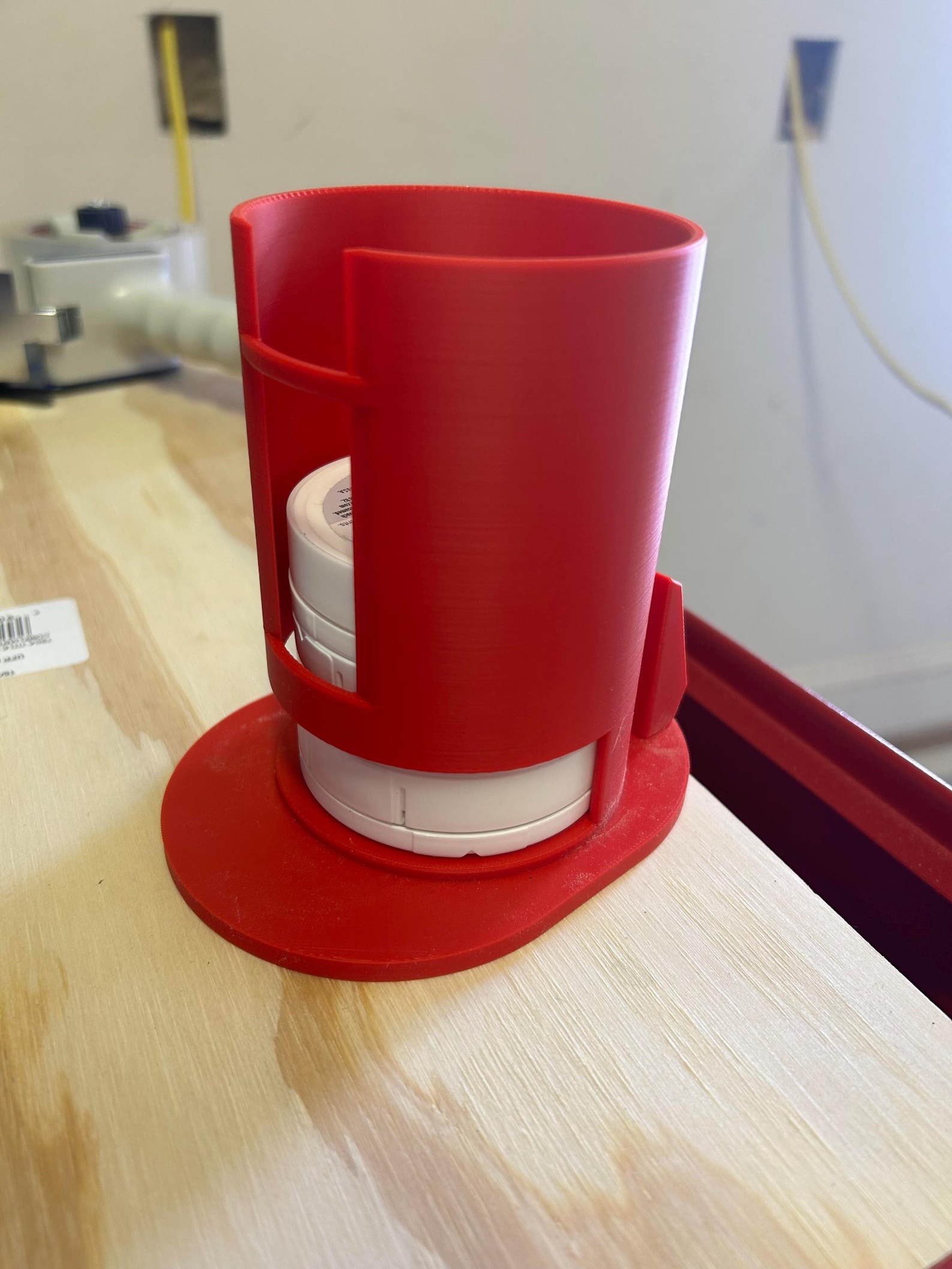 Red 3D-printed tabletop dispenser holding a stack of white round tins on a wooden workbench